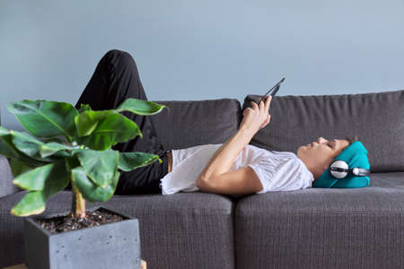Portrait of teenage boy 16 years old in headphones listening to music, audiobooks, lessons. Home interior indoor plants cacti potted backgroundの写真素材