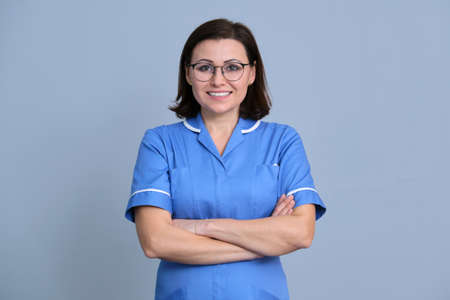 Portrait of confident smiling female nurse with arms crossed looking at camera, over gray backgroundの写真素材