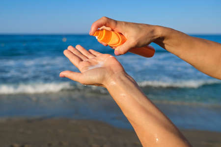 Bottle with sunscreen lotion in hands of woman on the beach, sea sky background. Skin protection creams with spf filter, summer sea vacationの写真素材