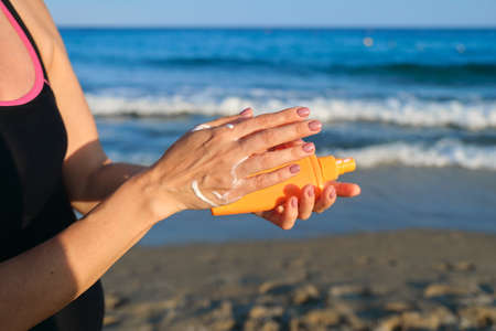 Close up of woman applying suntan lotion, sand beach blue sea background.の写真素材