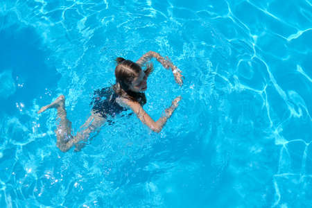 Kid has fun in an outdoor pool, child girl swims, dives, plays on the water, blue background. Childhood, holidays, summer, vacation conceptの写真素材