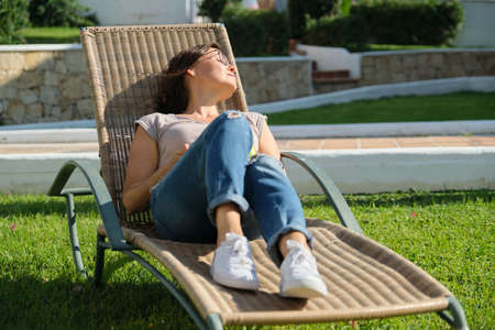 Mature adult woman resting lying in an outdoor chair on the lawn. Rest, relaxation, lifestyle, vacation, middle-aged peopleの写真素材
