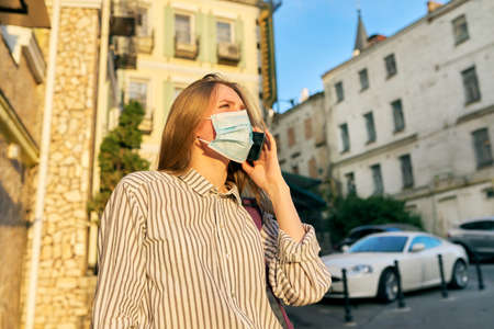 Young business woman in medical protective mask talking on smartphone outdoors. Business, pandemic, epidemic, healthcare and medicine, healthy lifestyleの写真素材