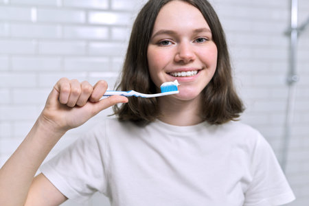 Close-up of teenager girl with toothpaste on brush brushing her teeth in the bathroom, morning and...