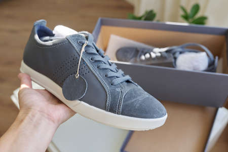 Men's fashionable gray leather sneakers, casual design. New pair of shoes unpacked from the box, shopping online, seasonal sales, men's shoe trends, box with sneakers at homeの写真素材