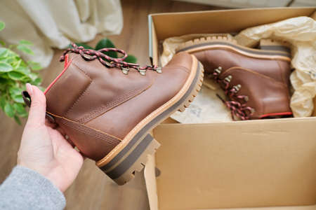 New womens leather brown waterproof hiking winter autumn boots in hands of female, trendy footwear for winter. Unpacking shoes, shopping online from home, shoe fashion storeの写真素材