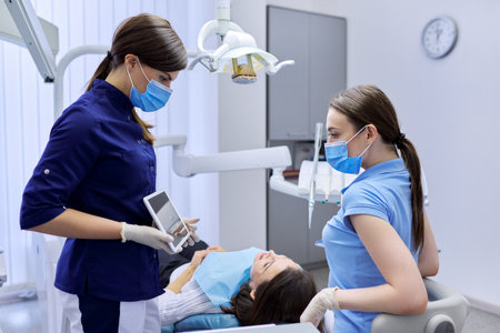 Dentistry, woman patient in chair in dental office, doctor colleagues consult looking in digital tablet. Medicine, dentistry and health care conceptの写真素材