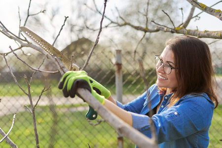 Spring pruning of trees and bushes in garden. Woman gardener in gloves with garden saw cuts...