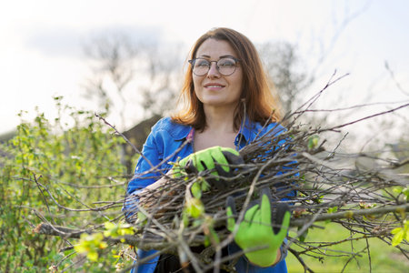 Spring pruning of trees and bushes in the garden. Woman gardener in gloves with dry branches of bushes and fruit trees. Hobby, gardening, farm conceptの写真素材