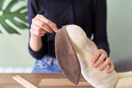 Teen girl sewing toy bunny doll sitting at home at table. Hobbies, leisure, lifestyle, handmade, creativity and adolescent skillsの写真素材