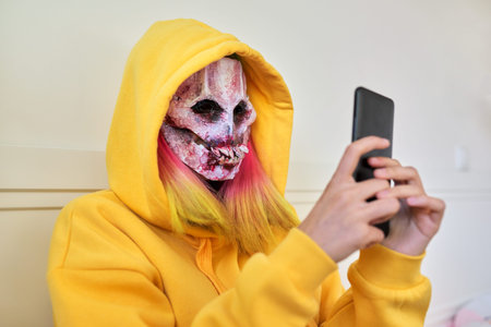 Halloween day, girl in scary nightmare face mask with hood on her head makes video call on...