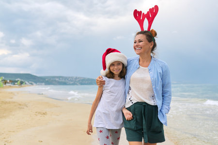 Happy mom and daughter child in Santa hat walking embracing on the beach. Family celebrating Christmas and New Year at tropical resort, copy space, vacations travel tourism conceptの写真素材