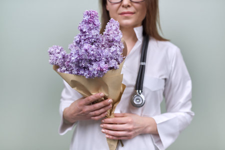 Bouquet of lilac flowers in the hands of woman doctor. Celebration, gift, respect and loveの写真素材