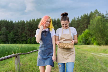Talking happy mother and teenage daughter walking together on country road with basket of fresh strawberriesの写真素材