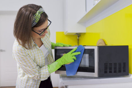 Woman in protective rubber gloves with rag cleaning microwave at home in the kitchenの写真素材