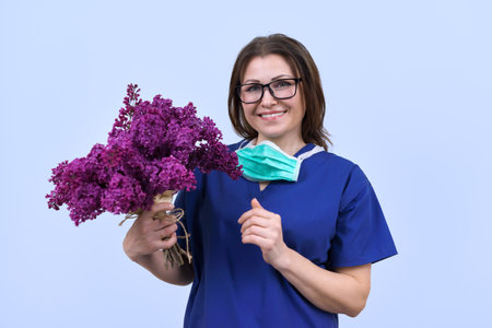 Portrait of mature smiling female doctor in glasses with protective medical mask holding bouquet of flowers. Doctors Day, World Health Day, National Nurses Dayの写真素材