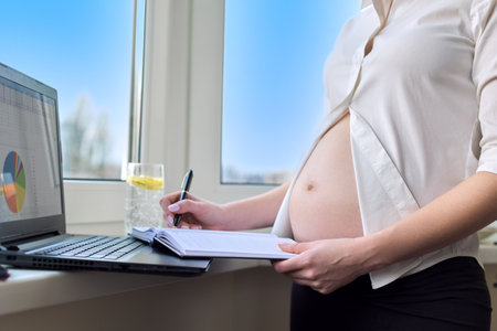 Young pregnant business woman working at home with laptop, window background. Remote work at home, pregnancy and businessの写真素材