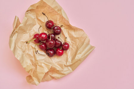 Ripe red cherry in craft paper, on a pink background, top viewの写真素材