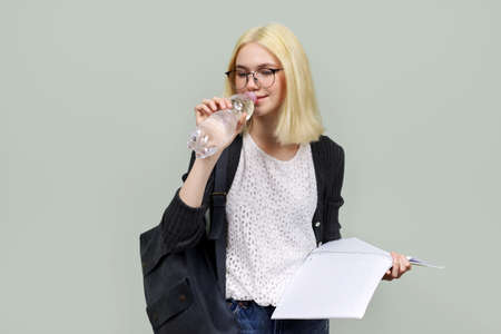 Young student teenager with backpack holding and drinking water from bottle on light green backgroundの写真素材