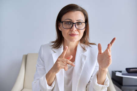 Positive talking middle aged business woman looking at webcam, recording video vlog webinar, making video business conference, popular counselor consulting online, female salesperson selling remotelyの写真素材