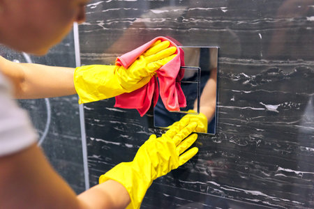 Bathroom cleaning, woman in gloves with detergent microfiber rag polishing tiles and chrome...