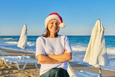Portrait of mature happy woman in santa hat on the beach sea resort, New Years Christmas holidays, tourism travel vacation people conceptの写真素材