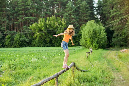Summer, nature, happiness, childhood concept. Girl in a hat walking on a rural wooden fence,...