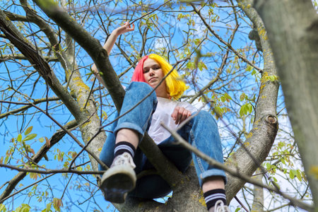 Teenager girl, hipster sitting high on a tree. Spring, nature sky background. Adolescence,...