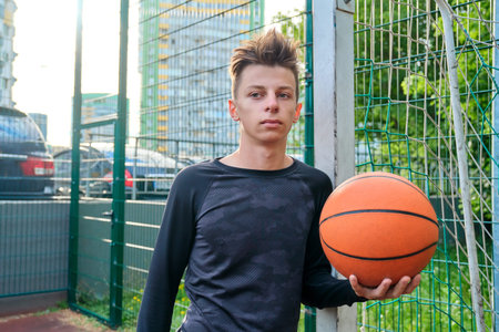 Guy teenager with basketball in his hands, outdoor basketball city court background. Active sports...