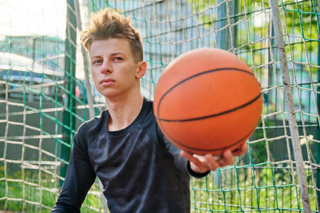 Close-up basketball ball in the hand of teenage guy, outdoor basketball city court background. Active sports healthy lifestyle of teenagers in the cityの写真素材