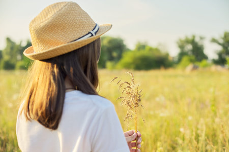 Summer nature, back view of child girl in straw hat tearing meadow grasses, copi space beautiful sunset meadow landscapeの写真素材