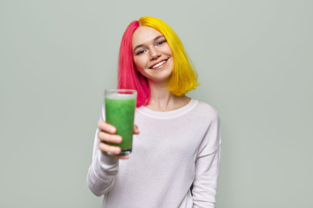 Fashionable teenager girl with glass of fresh green smoothies, on pastel background. Healthy food,...