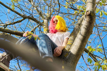 Teenager girl, hipster sitting high on a tree. Spring, nature sky background. Adolescence,...