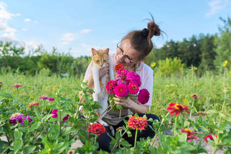 Mature happy woman with domestic cat and fresh zinnia flowers bouquet, summer natural landscape vegetable garden backgroundの写真素材