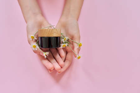 Medical herbal natural cosmetics with chamomile. Woman hands, flowers and glass bottle with product on pink background, top viewの写真素材