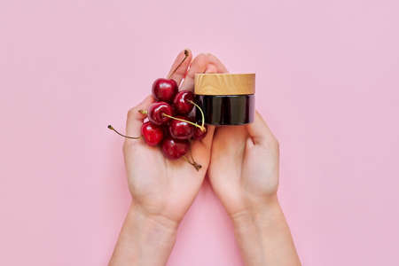 Natural healthy organic cosmetics, womans hands, fruits, cherries, bottle with cosmetic product on pink background. Cosmetology, treatment, skincare, therapyの写真素材