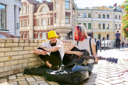 Happy young people couple guy and girl playing acoustic guitar. Trending creative teenagers sitting...