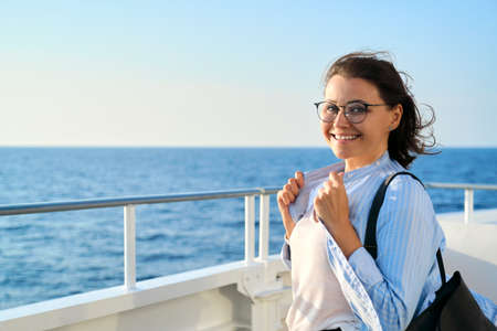 Happy middle aged woman on deck of cruise ship, copy space blue sky sea sunset. Smiling mature female looking at the cameraの写真素材
