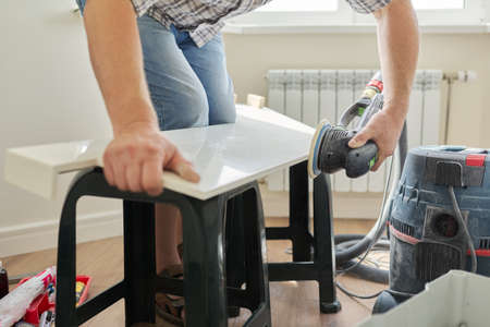 Artificial stone window sill, installation, technological process. Repair, construction of a house, apartment. Close-up shot of a builder grinds a window sill using a grinderの写真素材