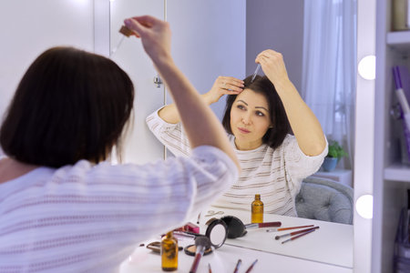 Mature woman treating caring for hair using cosmetic medical products in bottle with pipette....