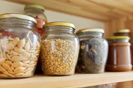 Kitchen pantry, wooden shelves with jars and containers with food, food storage. Jars with sunflower seeds, pumpkin seeds, oatmealの写真素材