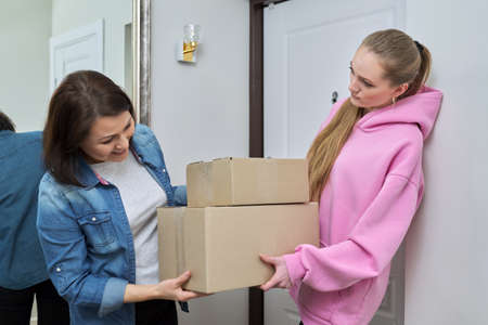 Delivery of goods, social services, post, home, lifestyle, online shopping. Two women with cardboard boxes near the front door of the houseの写真素材
