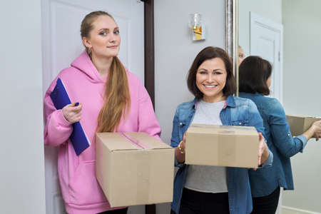 Delivery of goods, social services, post, home, lifestyle, online shopping. Two women with cardboard boxes near the front door of the houseの写真素材
