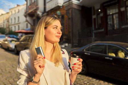 System of heating tobacco, paper cup of coffee in hands of woman on city street
