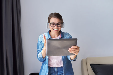 Middle aged woman in headphones with digital tablet at home on armchair