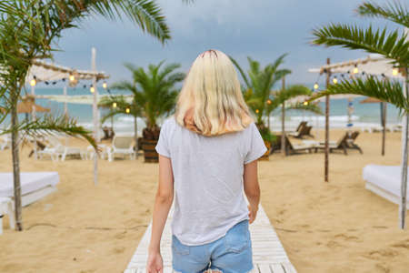 Young beautiful woman walking along evening beach, back viewの写真素材