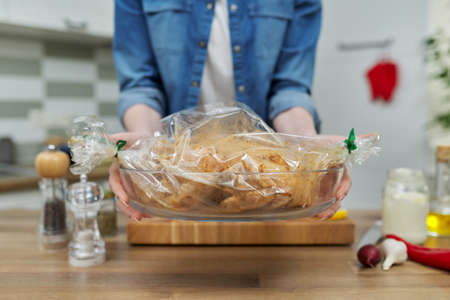 Marinated chicken in bakery cooking bag for roasting and hands of womanの写真素材