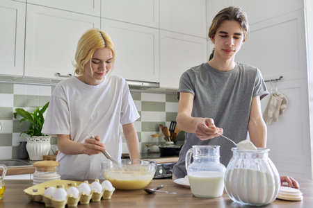 Teenagers guy and girl cooking pancakes in kitchen togetherの写真素材