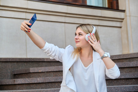 Young beautiful woman in headphones with smartphone resting sitting on steps in city