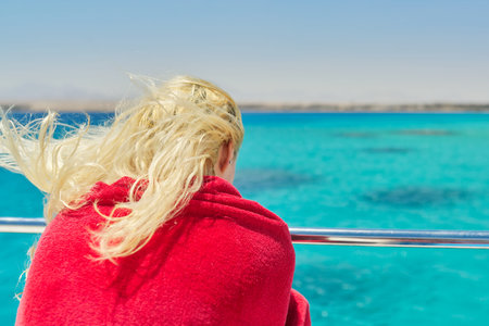 Young blonde female on yacht looking at turquoise coral reefs in Red Sea